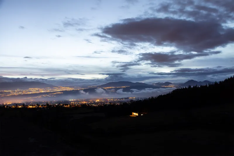 Distant view of the illuminated building on a dark slope above a lit valley at dusk
