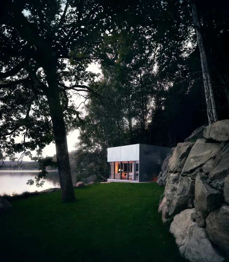 Illuminated pavilion on a lawn clearing between rocky outcrops and tree canopy at twilight