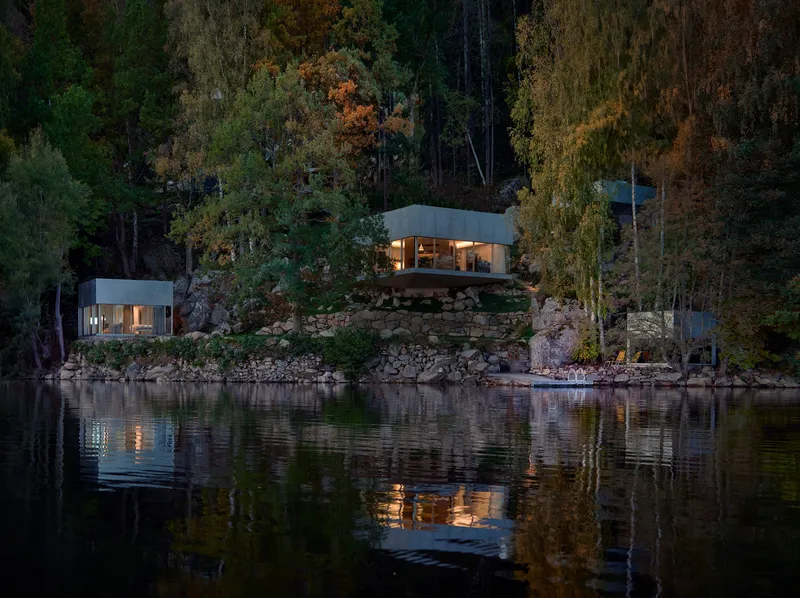 Three pavilions on a rocky lakeside slope illuminated at dusk with reflections in the still water