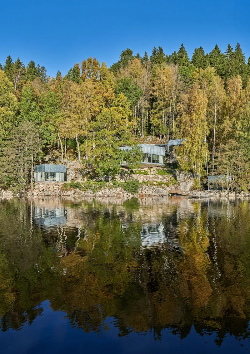 Three glass pavilions nestled among boulders and autumn trees reflected in the calm lake surface