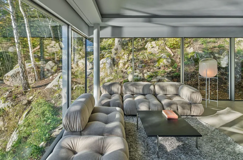 Living room with grey seating and full-height glazing overlooking the rocky wooded slope