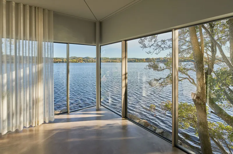 Corner room with floor-to-ceiling windows overlooking a lake and tree branches in afternoon light