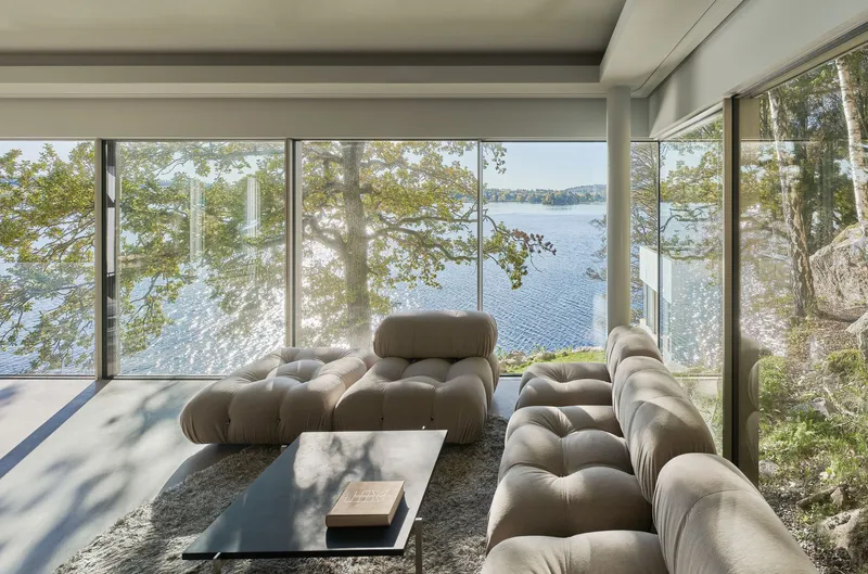 Living room with full-height glazing framing lake views and dappled shadows from overhanging oak branches