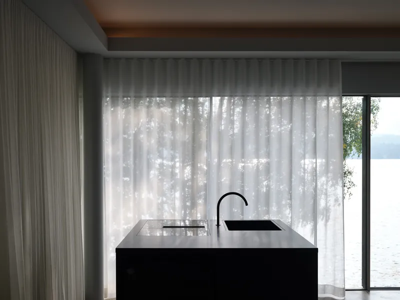 Black stone kitchen island with integrated sink against sheer curtains filtering daylight from the lake