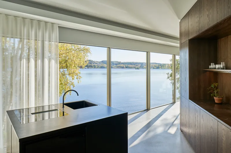 Kitchen with black island and timber cabinetry facing a wall of glass overlooking the water