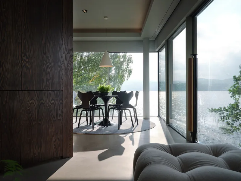 Dining area with floor-to-ceiling glass overlooking a misty lake framed by trees