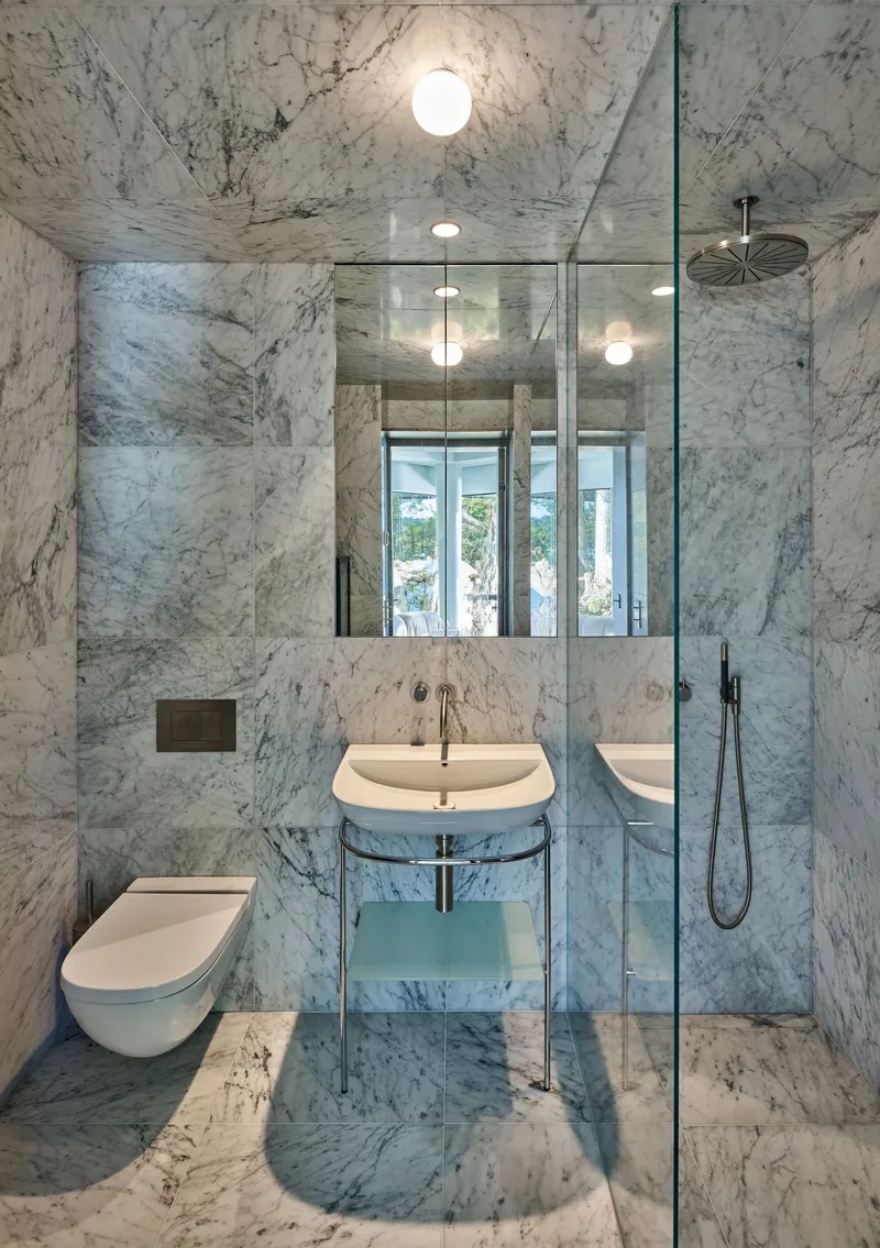 Bathroom clad entirely in white veined marble with glass shower enclosure and globe pendant lights