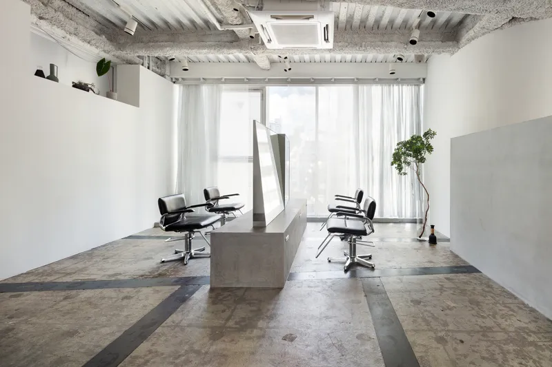 Salon workspace with concrete stations and sheer curtains filtering light from the window wall