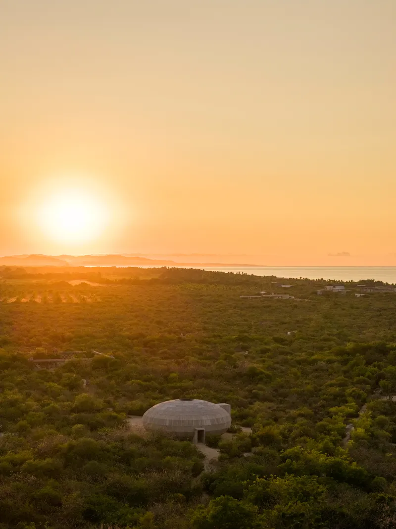 Elevated view of oval dome accessed by footpath through scrubland with ocean and sunrise beyond