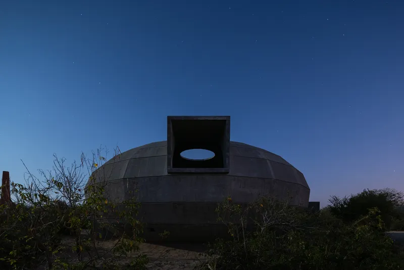 Concrete dome with a central chimney opening framed by an oval oculus at dusk