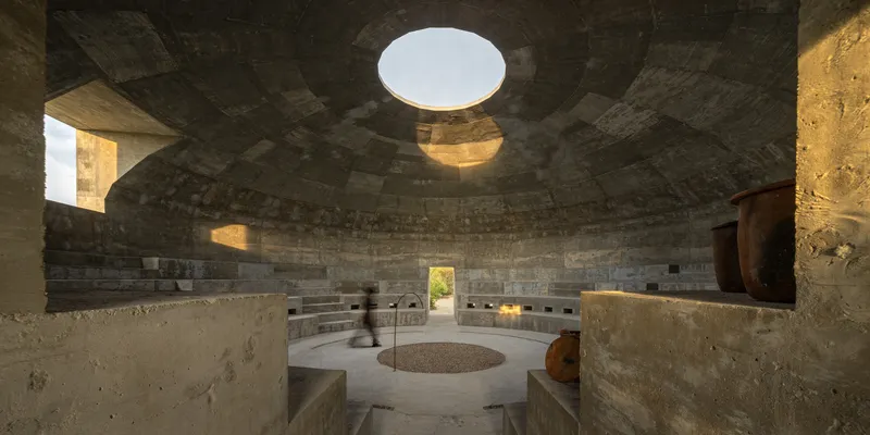 Interior of circular concrete chamber with tiered seating and central oculus casting afternoon light