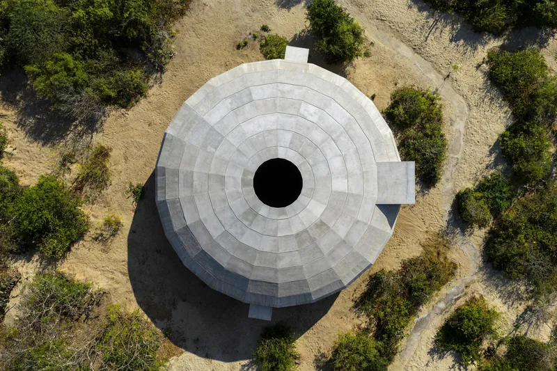 Drone view of the circular concrete roof with central oculus surrounded by dry grassland and scattered trees