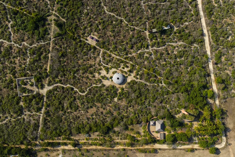 Aerial view showing two circular structures connected by dirt paths through dense scrubland vegetation