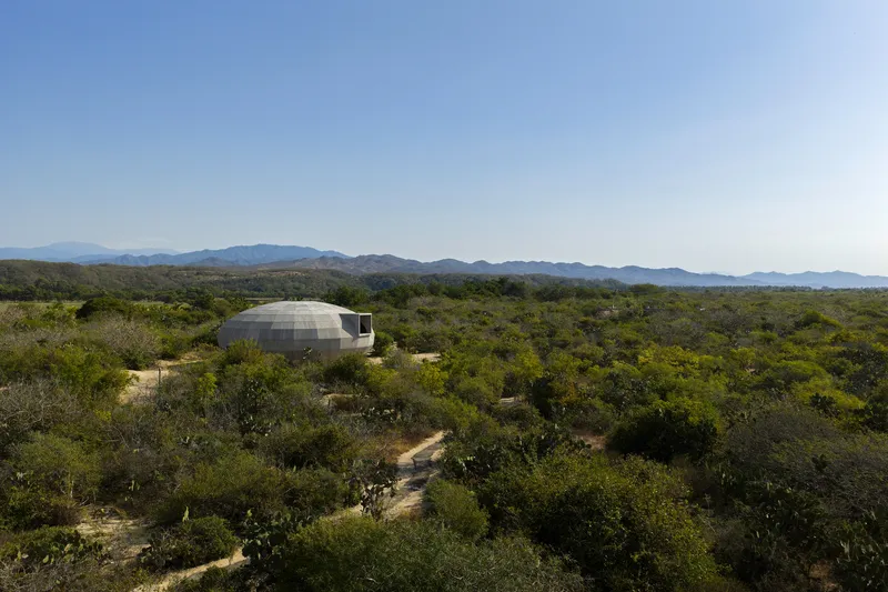 Domed concrete structure nestled in arid landscape with distant mountain ranges under clear sky