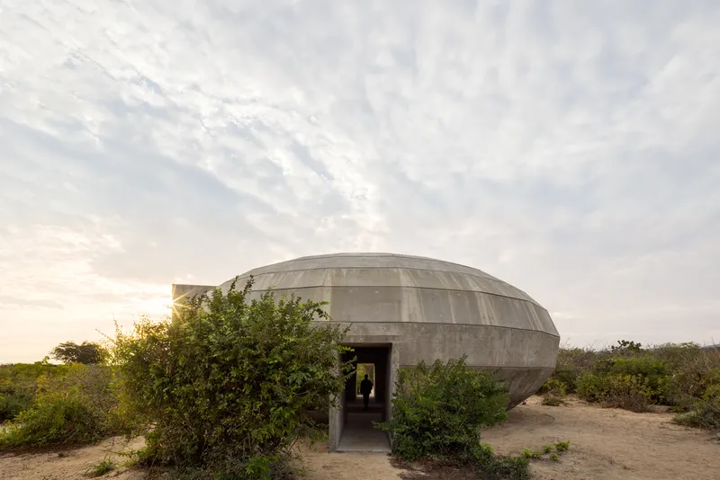 Entrance to the concrete dome with flanking shrubs at dusk under soft cloud cover