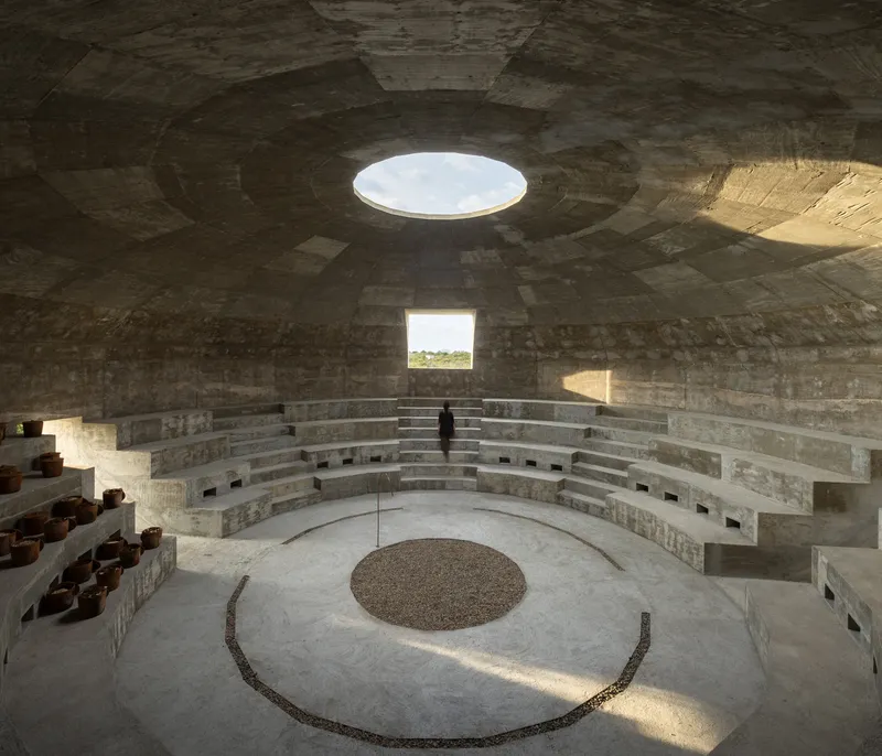 Interior amphitheater with concentric seating rings beneath a circular skylight and framed landscape opening