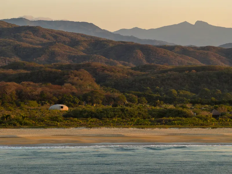 Distant view of the dome from the beach at golden hour with layered mountains beyond