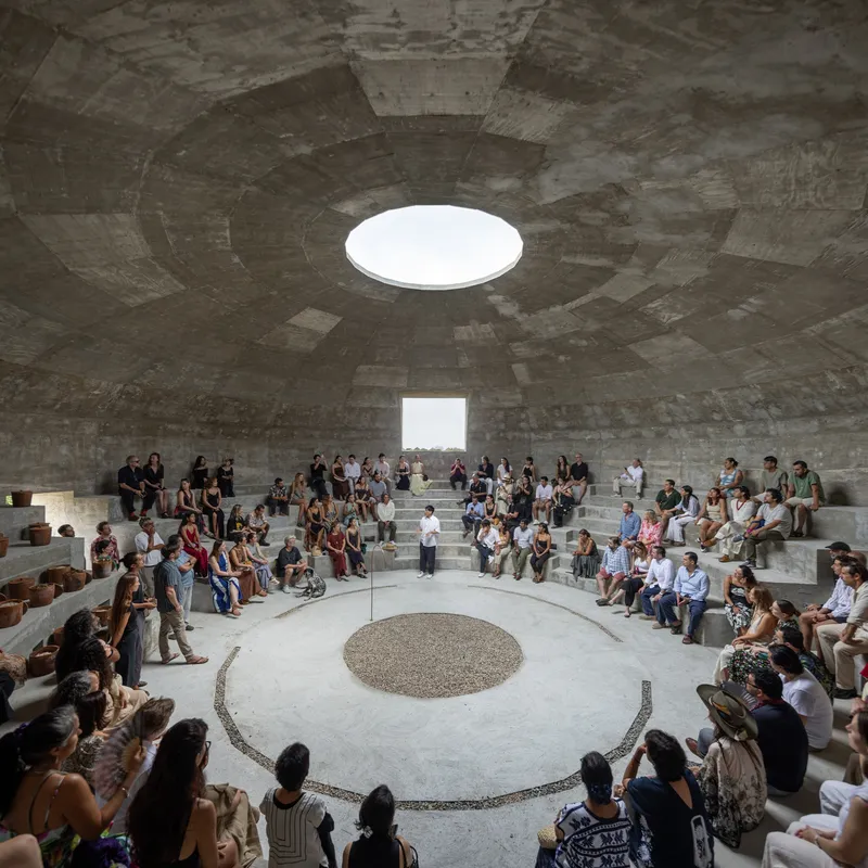 Amphitheater seating filled with visitors gathered around a gravel circle beneath the open oculus