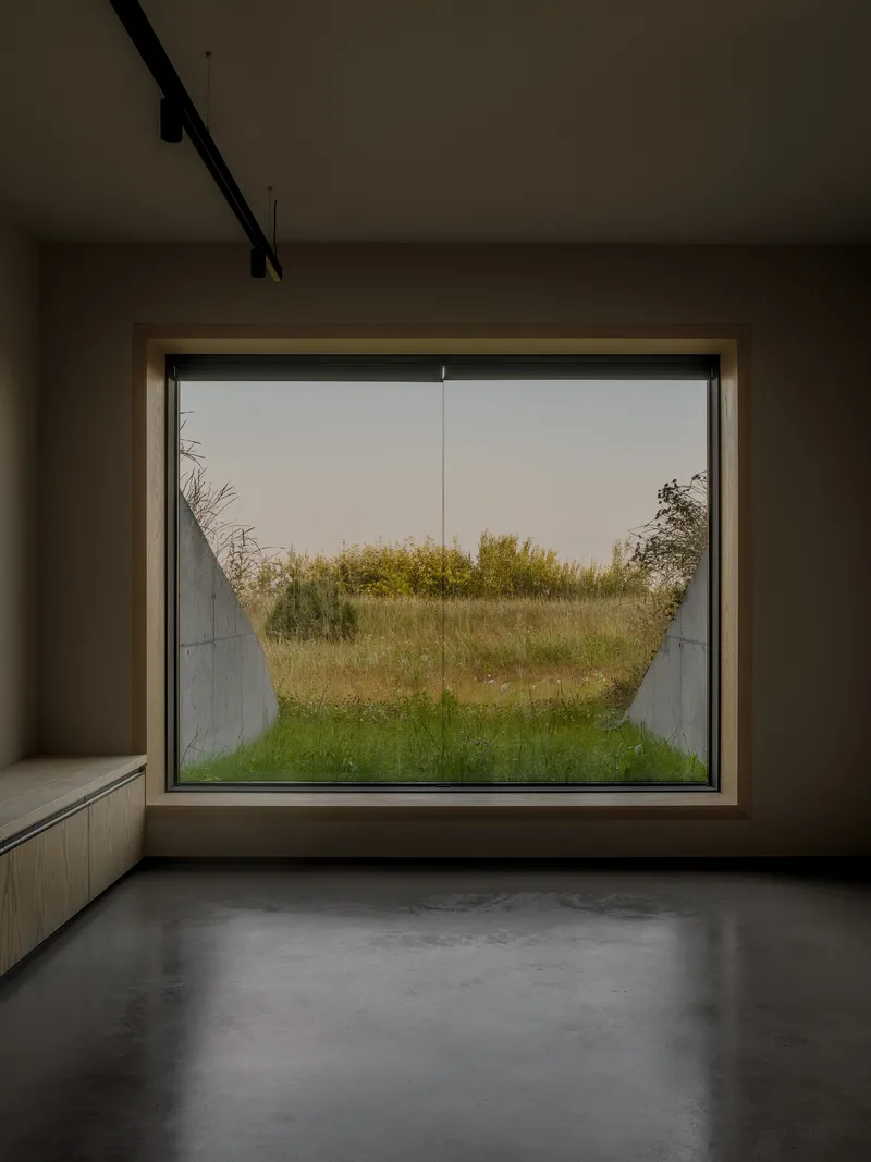 Large picture window framing a view of prairie grasses beneath an overcast sky
