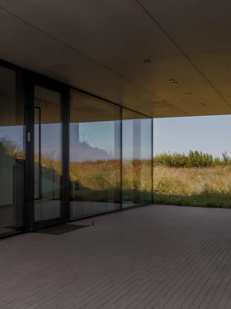 Covered timber deck with sliding glass doors opening to a grassy hillside at dusk