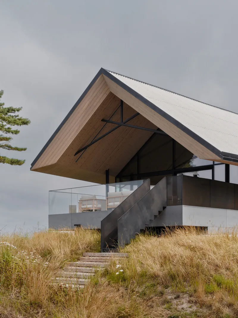 Cantilevered roof over concrete stair leading through dry coastal grasses under stormy skies