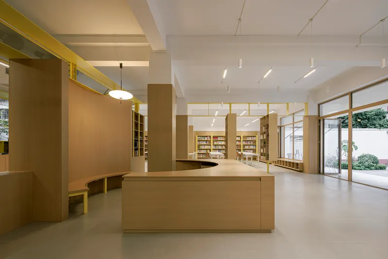 Central timber service counter beneath yellow ceiling beams with glazed doors opening to a courtyard beyond