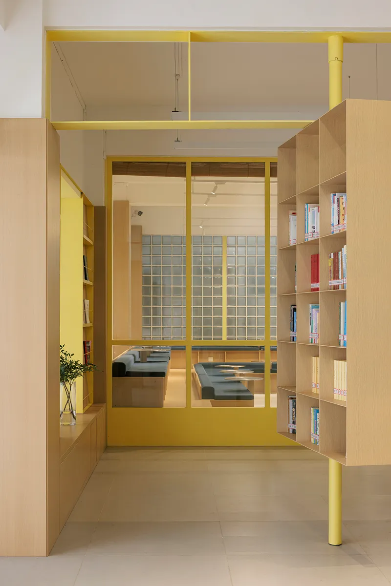 Yellow steel frame enclosing a reading nook with built-in bench and glass block wall