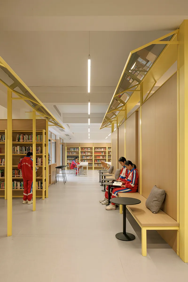 Library corridor with yellow steel structural frames and seated readers in red uniforms