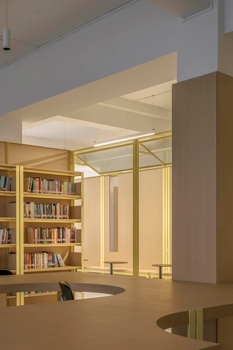 View through yellow steel columns toward bookshelves and glazed opening with evening light