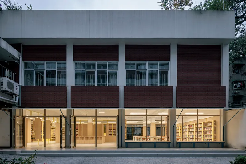 Street-facing facade with alternating bands of dark brick panels and full-height glazing at dusk