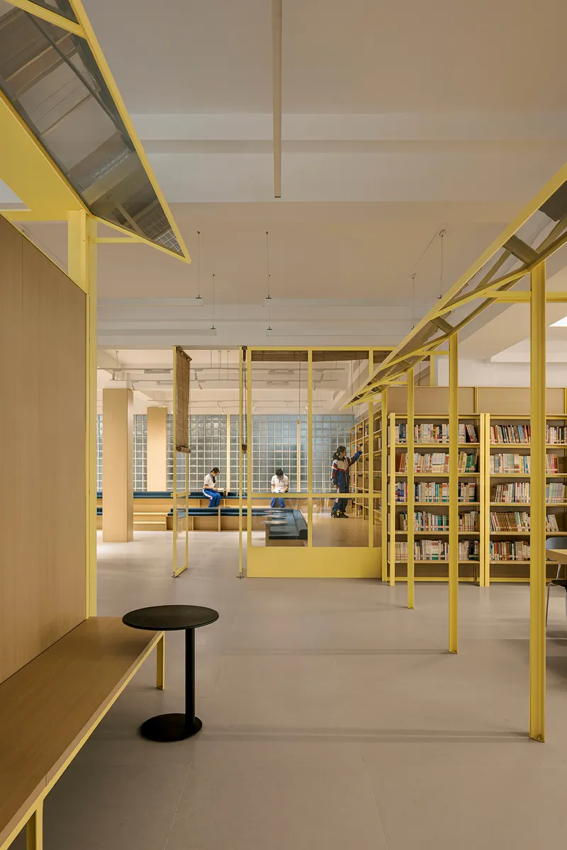 Reading area framed by yellow steel columns and beams with visitors seated on benches beneath pendant lights