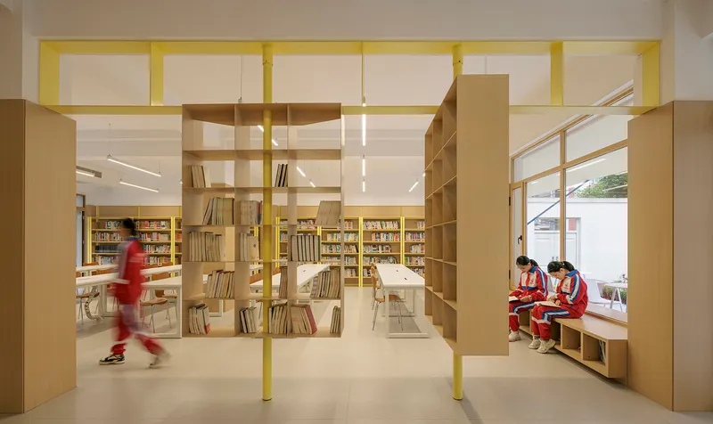 Library interior with a student walking past timber shelving and yellow steel framework near window seating