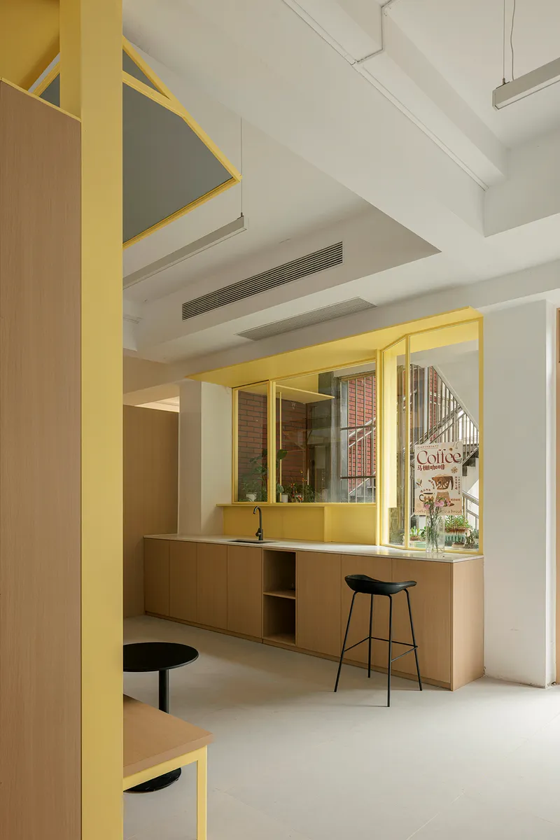 Service counter with timber cabinetry and black stools beneath a yellow steel framed opening with mirror