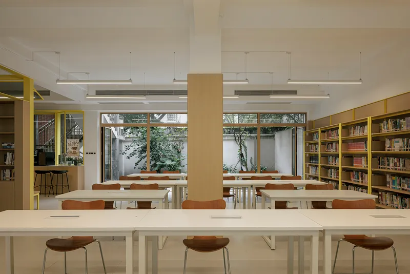 Reading room with white tables and timber stools facing courtyard windows framed by planters and trees