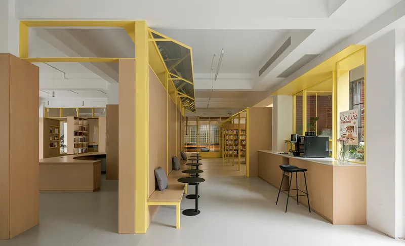 Long view through yellow steel frames organizing light timber counters and shelving in a bookshop interior