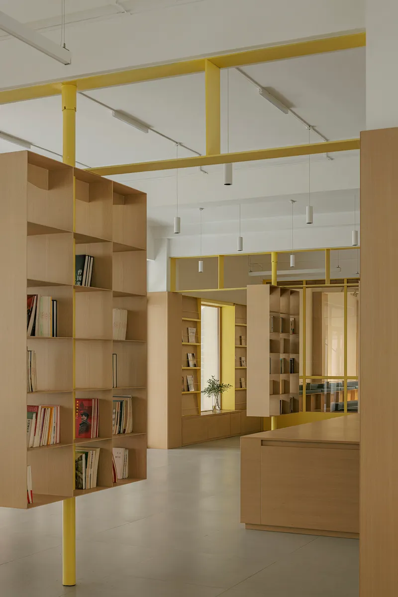 Light timber shelving units beneath yellow steel portal frames with cylindrical pendant fixtures overhead