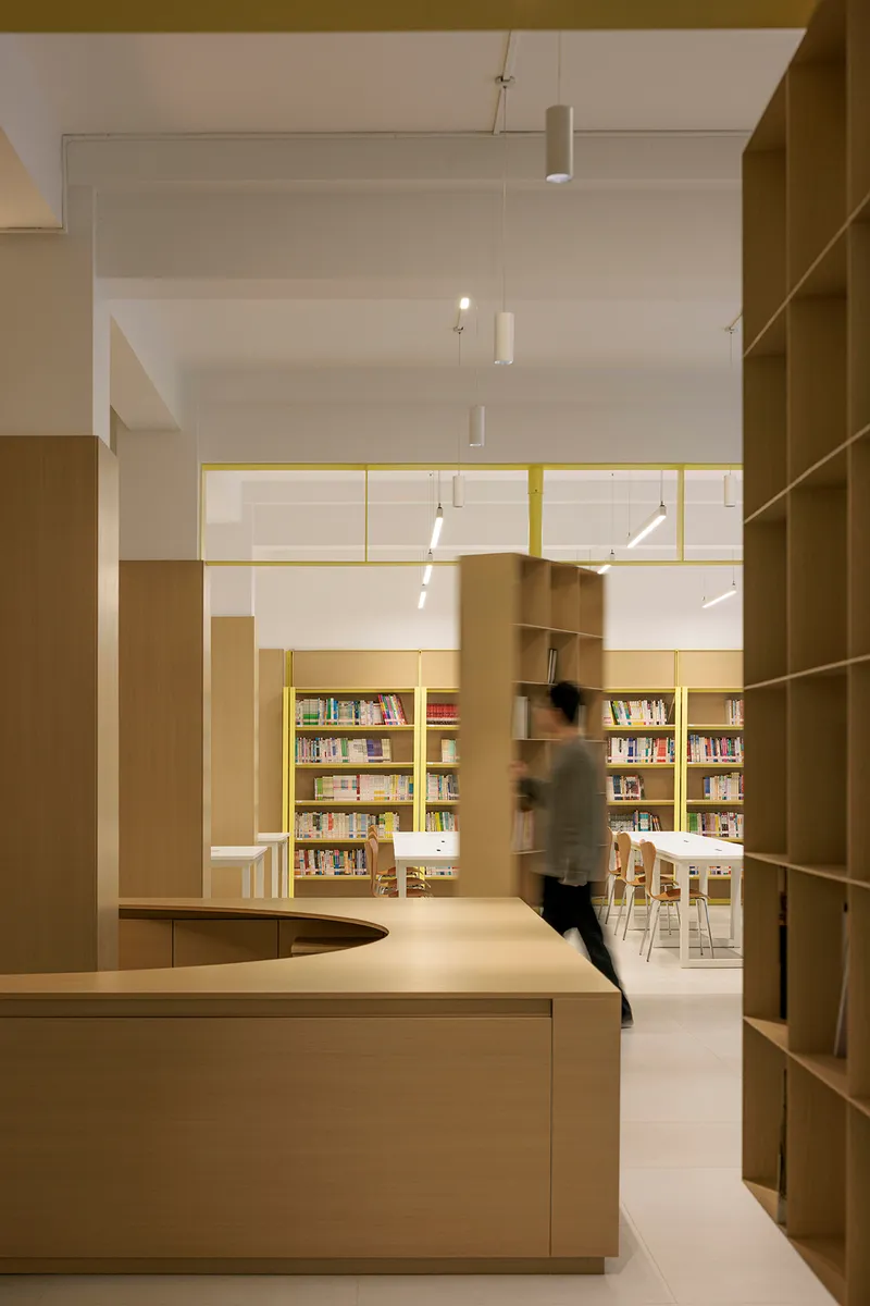 Framed view through yellow steel portals toward a reading area with a figure in motion