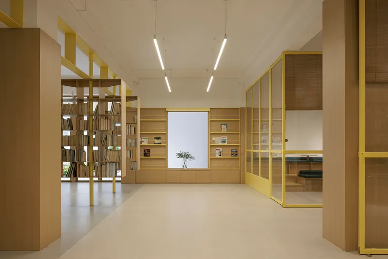 Library interior with yellow metal frame shelving and timber cabinetry under linear ceiling lights