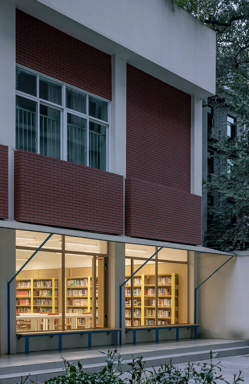 Facade detail showing maroon brick panels and illuminated ground floor windows at dusk