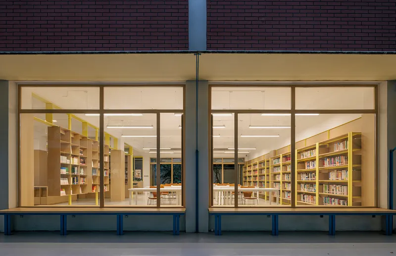 Storefront glazing revealing library shelves and reading tables under evening light