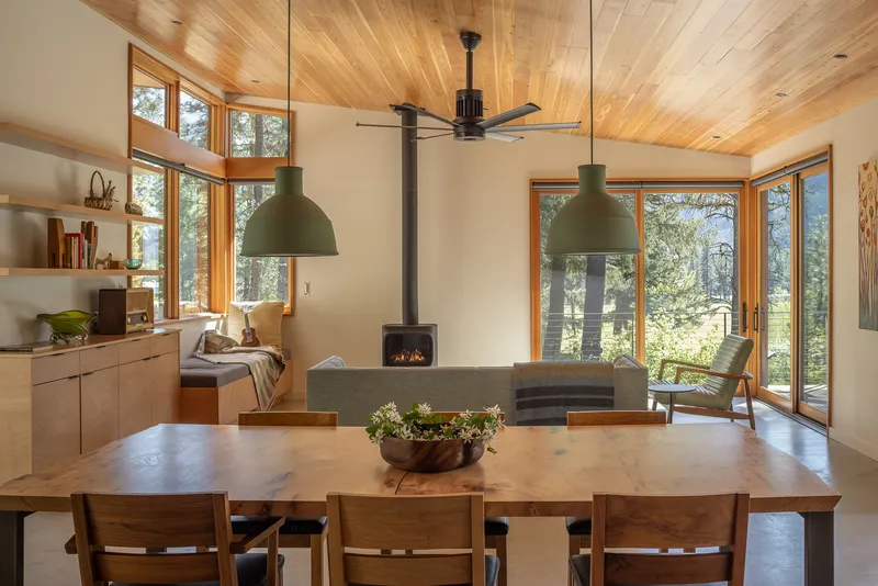 Open living and dining space with wood-burning stove beneath vaulted timber ceiling and clerestory windows