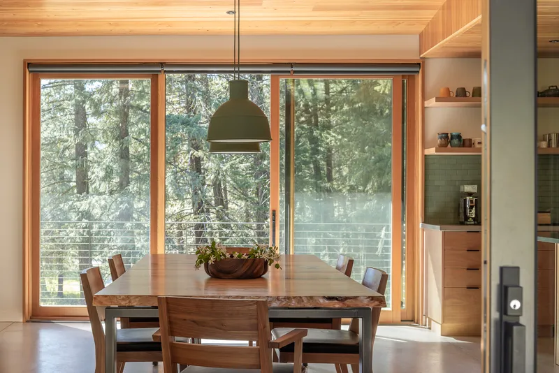 Dining area with timber ceiling and large glazed doors overlooking a winter forest