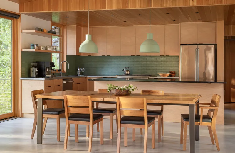 Open kitchen with green subway tile backsplash and light wood cabinetry beneath pale pendant fixtures