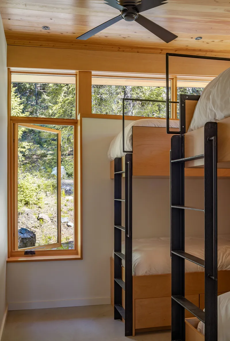 Bunk room with steel ladder frames and timber-clad walls beneath a ceiling fan
