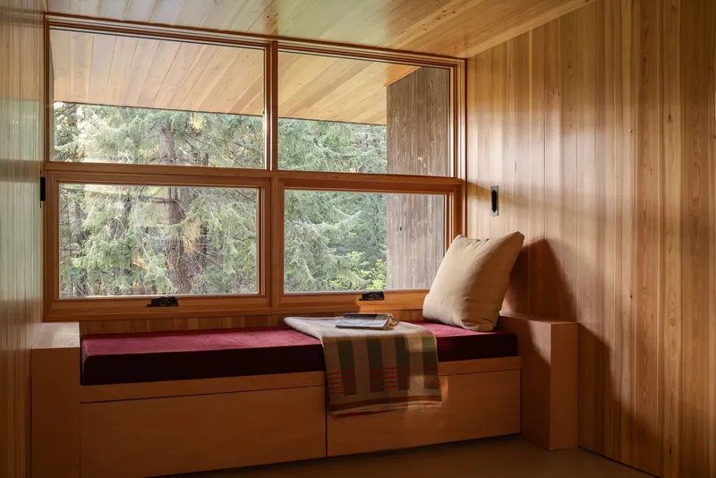Built-in window seat with storage drawers beneath transom windows framing forest views