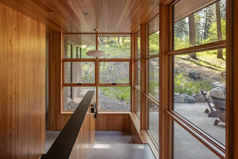 Glass-walled hallway with timber cladding leading to an outdoor patio and gravel landscape