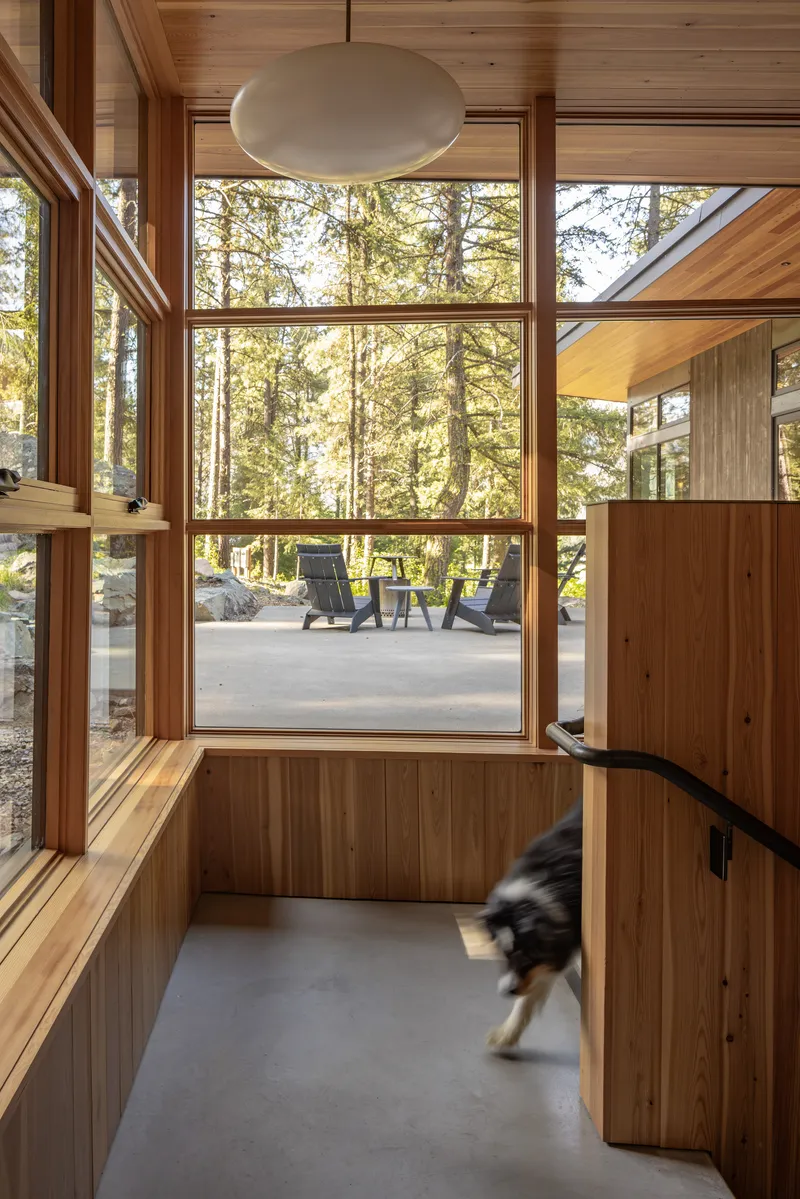 Wood-paneled interior corner with floor-to-ceiling glazing framing a view of the terrace and forest