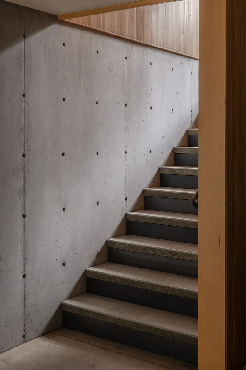 Timber and steel staircase ascending alongside a board-formed concrete wall with tie holes