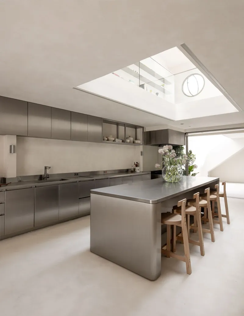 Kitchen island with timber stools under an angled skylight casting afternoon shadows
