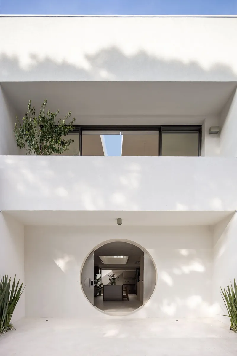 White stucco facade with circular entry portal framing the kitchen island under cloudy skies